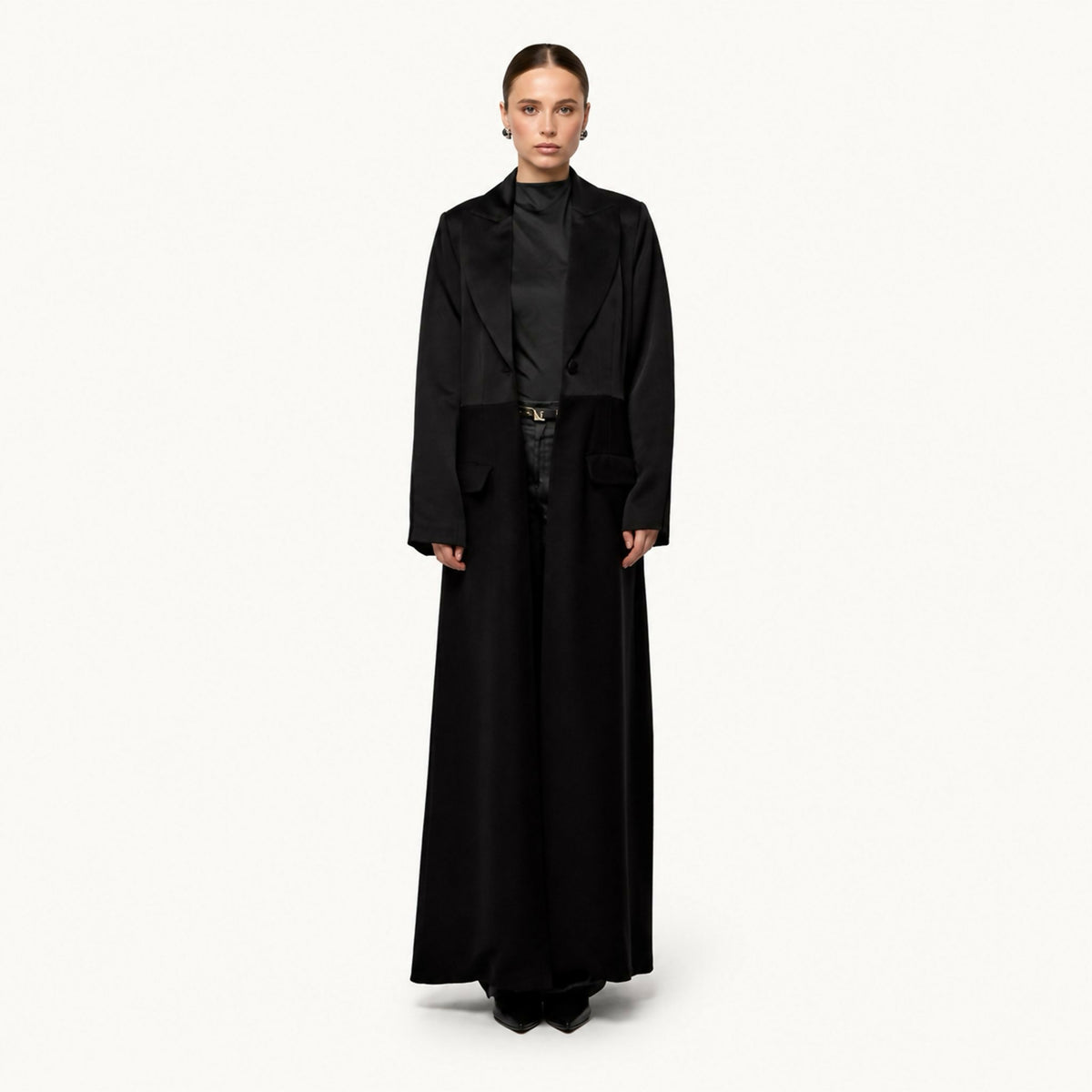 Tailored open-front coat-style abaya with a satin notched lapel, fitted waist seam, and flap pockets, worn over trousers.