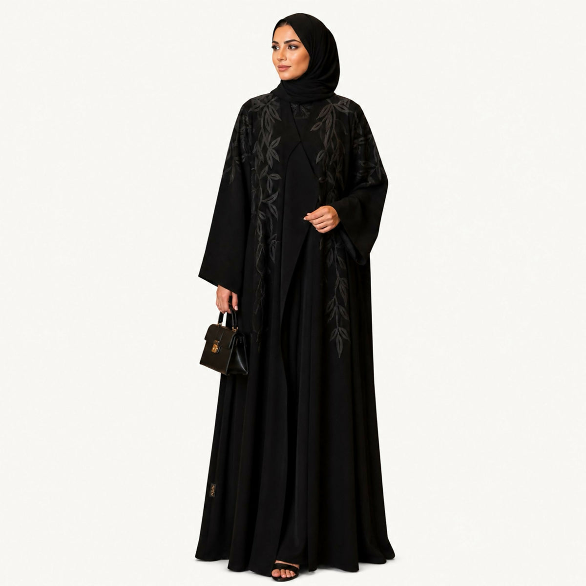 Black crepe abaya with a front panel featuring squares with black embroidery and hand-perforation on the front and back. Fabric works for both summer and winter; hand wash or steam clean.